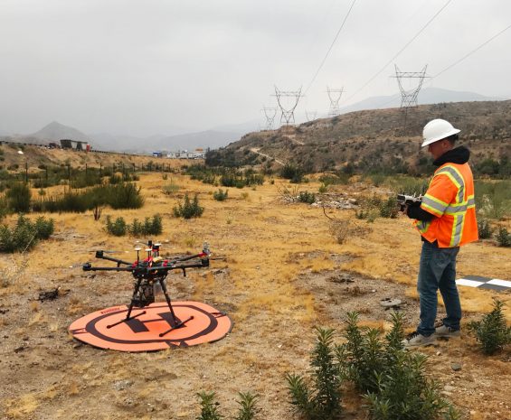 Drone pilot looks at UAV on a ground target, with energy transmission lines in the background.