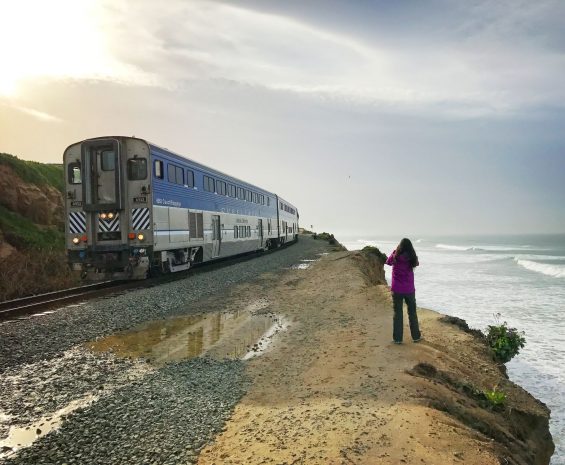 Girl photographs a passing train while standing on a coastal bluff in San Diego.